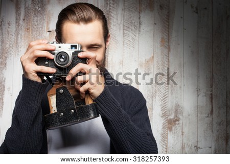 Handsome photographer is making photos with aspirations. He is standing and holding camera. The hipster with beard is smiling. Copy space in right side
