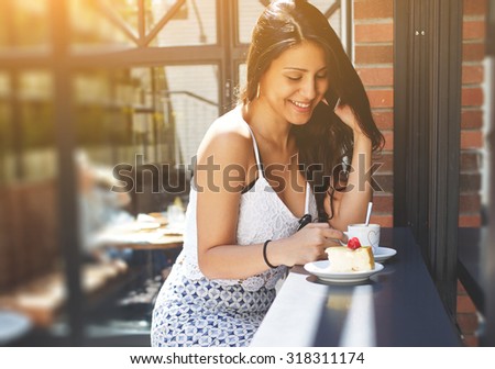 Portrait of young pretty female with excellent figure in elegant summer clothes talking on cell phone while sitting in a coffee shop, gorgeous woman laughing at smart phone conversation, flare sun