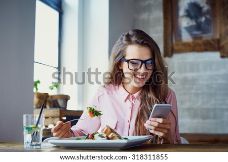 Young woman eating salad at restaurant and texting on smartphone Royalty-Free Stock Photo #318311855