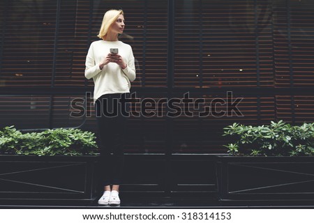 Full length portrait of gorgeous young woman holding smart phone in hand and looking to the empty copy space area for your text message or information,female hipster have chat conversation on phone
