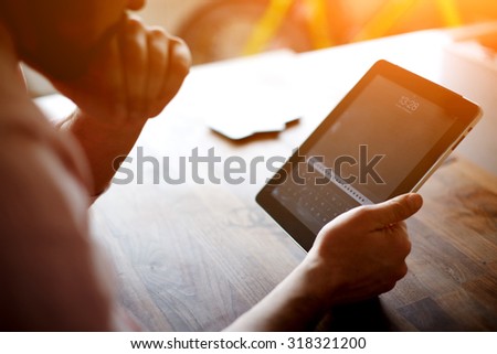Thoughtful business man looking to the digital tablet screen while sitting in modern loft interior at wooden table,entrepreneur or freelancer work on touchscreen pad at the office,flare sun and filter