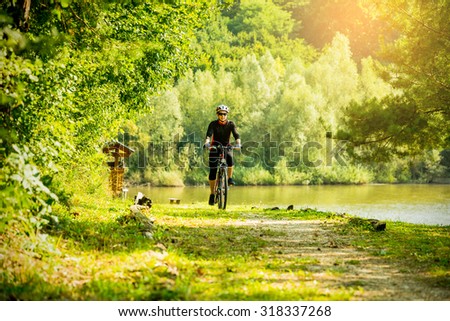 Young woman riding a bike in the forest next to a lake at sunset. Royalty-Free Stock Photo #318337268