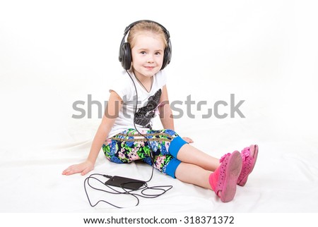 Cute beautiful little girl sitting on white background and listening to music on headphones