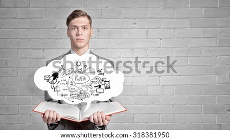 Young businessman with opened book in hands blowing on pages
