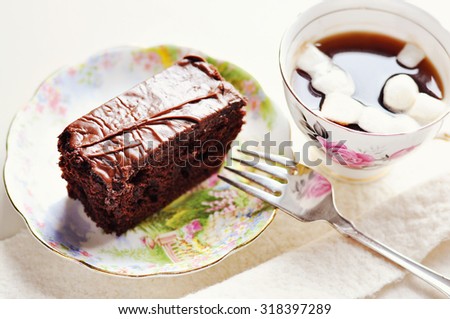 Chocolate cake on a porcelain plate and a cup of coffee with marshmallows. Selective focus