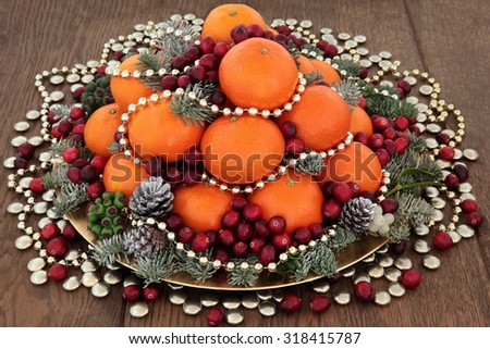 Christmas satsuma orange and cranberry fruit, gold bead and smartie decorations, holly, mistletoe and winter greenery over oak background.