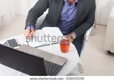 Businessman in office sitting at a table with a laptop writes with concentration