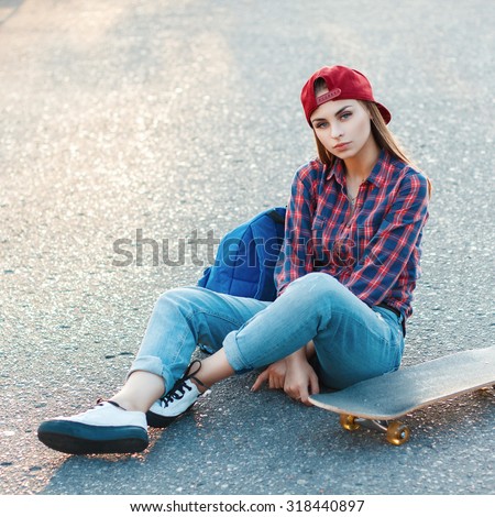Beautiful young girl sitting on the asphalt with a skateboard. Outdoor lifestyle picture on a sunny summer day