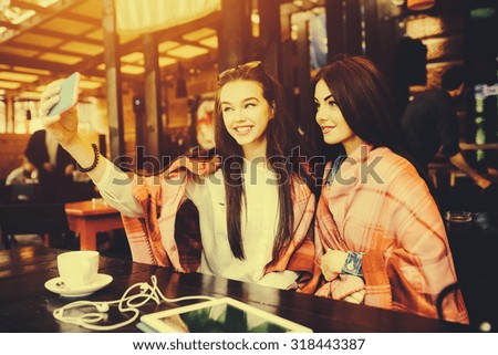 Two young and beautiful girl sitting at the table and doing selfie in the cafe