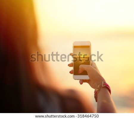 Tourist hand holding smart phone and taking photo of beautiful beach sunset