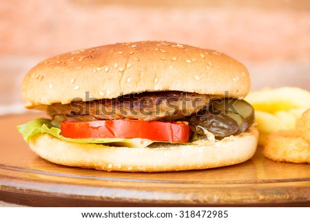 Classic homemade hamburger with onion rings and french fries on a wooden plate. Juicy homemade food. Horizontal, macro