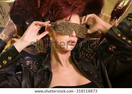 Studio photo of a young girl with red hair wearing glasses with gold spikes in the style of fashion and rock, on a shimmering background