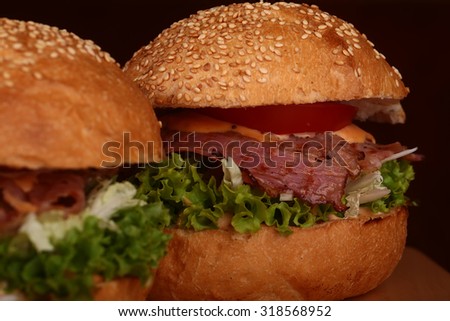 Few appetizing big delicious fresh burgers with green lettuce red tomato cheese cabbage bacon slice meat cutlet and white bread bun with sesame seeds on black background closeup, horizontal picture