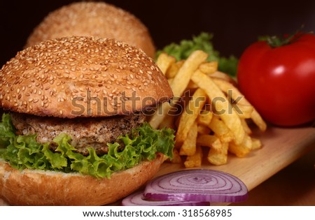 Big tasty appetizing fresh burger of green lettuce red tomato cheese and bacon slice meat cutlet and white bread bun with sesame seeds chips and violet onion closeup, horizontal picture