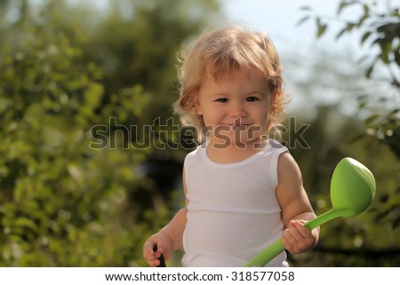 Portrait of happy smiling boy with blond curly hair in white underwear holding plastic ladle looking forward outdoor sunny day on natural background, horizontal picture