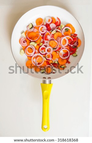 Picture of pan full of fresh vegetables, such as: onion, carrot, Bulgarian pepper etc. Modern pan with yellow handle.