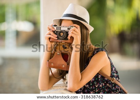 Young beautiful woman in hat is taking picture with old fashioned camera, outdoors.