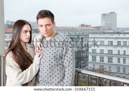 Portrait of handsome couple, man and woman, in embracing pose on outside balcony , city background of trees and buildings. Fancy female and male, lovers on terrace. Fashion lifestyle photo.