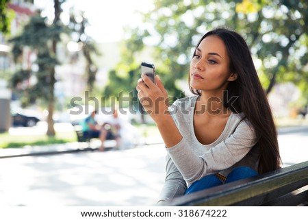 Portrait of a beautiful woman using smartphone on the bench outdoors