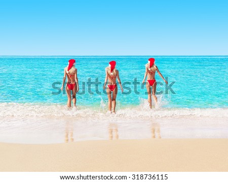 Beautiful young blonde Women in christmas hats on ocean beach running to waves. New year or Christmas holidays in hot countries concept.