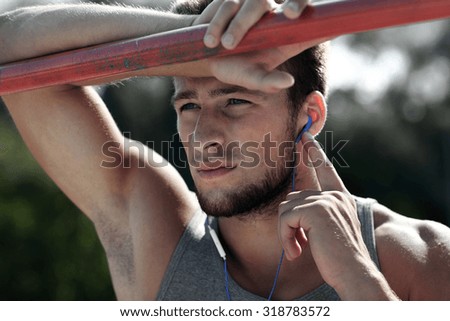 fitness, sport, training and lifestyle concept - young man with earphones listening to music and exercising on horizontal bar outdoors