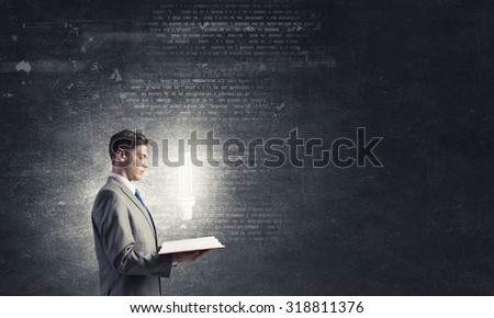 Businessman holding opened book with glass glowing light bulb 