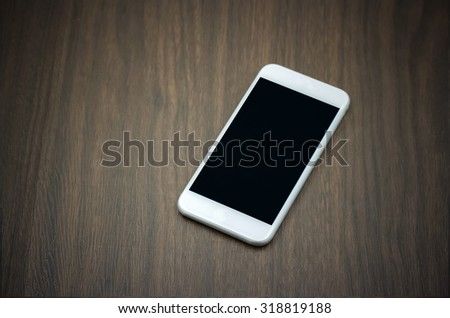 Smart phone in white color with blank screen laying on wooden table - vintage filter effect