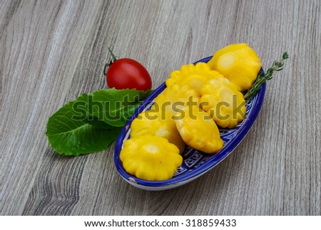 Yellow Pickled patissons with thyme leaves on the wood background