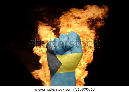 fist with the national flag of bahamas near the fire on a black background