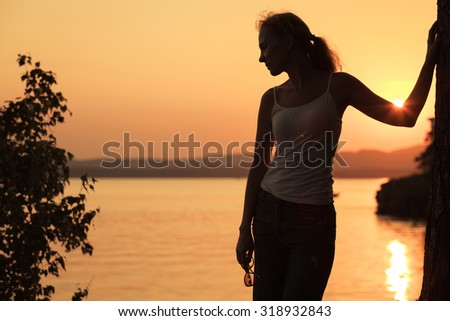 Silhouette of woman who standing on the coast of lake at the sunset time. 