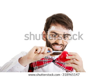 Determined man wearing suspenders cutting heart model with scalpel..