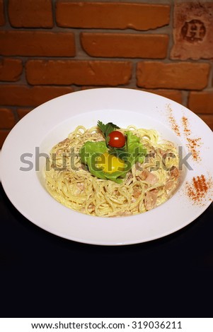Tasty classical pasta carbonara with bacon egg yolk parmesan cheese decorated with leaf lettuce and red cherry tomato on white round plate closeup, vertical picture