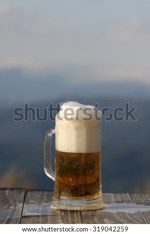 One glass mug with lager or porter tasty frothy beer on wooden table top sunny day outdoor on natural with mountain hills and yellow dry grass background, vertical picture