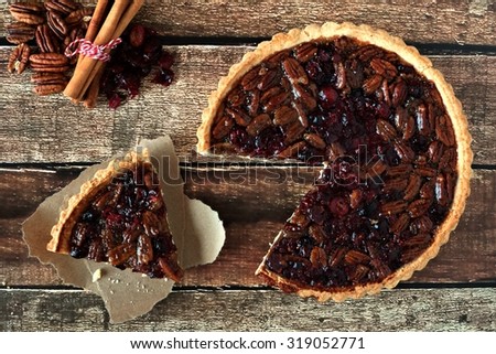 Pecan and cranberry autumn pie, overhead table scene with cut slice on rustic wood