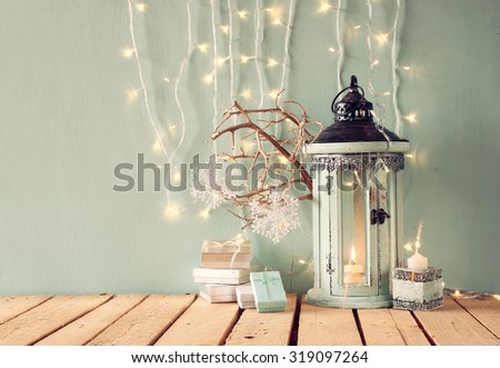 white wooden vintage lantern with burning candle, christmas gifts and tree branches on wooden table. retro filtered image
