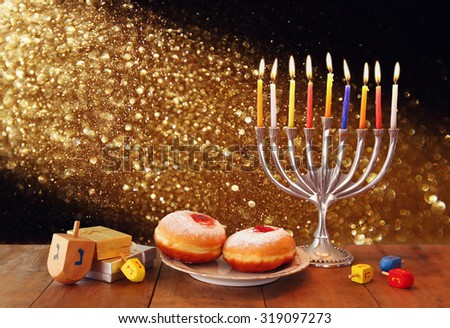 low key image of jewish holiday Hanukkah with menorah, doughnuts and wooden dreidels (spinning top). retro filtered image
