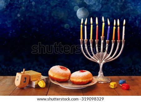 low key image of jewish holiday Hanukkah with menorah, doughnuts and wooden dreidels (spinning top). retro filtered image
