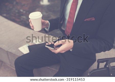 Cropped image of business person drinking coffee and checking messages on his phone