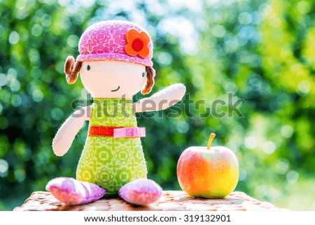 Plush doll sitting near apple