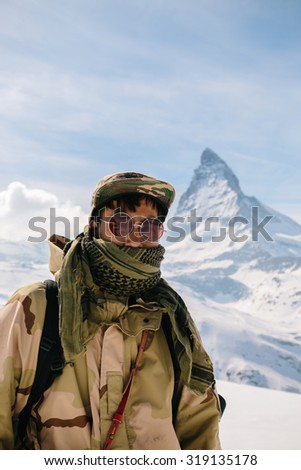 A man in camouflage winter coat standing in front of the background of Matterhorn.