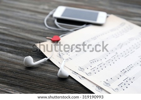 Mobile phone and earphones with music notes on wooden background