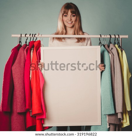 Happy smiling pretty woman in wardrobe holding blank empty banner. Gorgeous girl customer in mall shop with copyspace. Fashion clothing sale advertisement concept. Instagram filter.