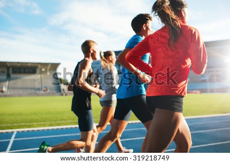 Rear view of young people running together on race track. Young athletes practicing a run on athletics stadium track. Royalty-Free Stock Photo #319218749