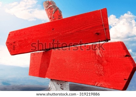 Red wooden direction arrows on top of the mountain, against clear sky.