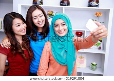 portrait of three beautiful women taking photos with smartphone camera