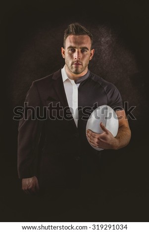 Tough rugby player holding ball against half a suit