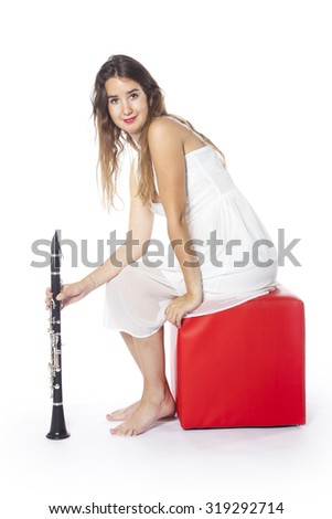 young brunette woman dressed in white sits on red stool in studio and holds clarinet smiling