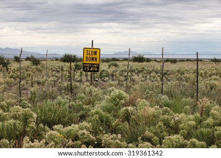 Yellow warning speed limit sign on countryside fence in overcast weather/Yellow SLOW DOWN Sign on Wild Rural Field Fence in Cloudy Weather/Yellow warning speed limit sign on country fence