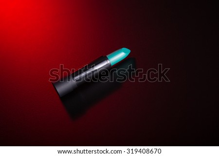 Teal green lipstick on red background, studio shot 