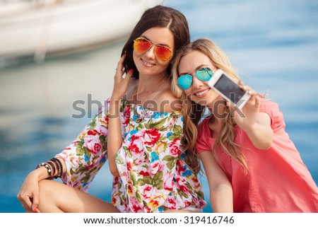 Beautiful girls with shopping bags taking a "selfie" with their cell phone. sale, consumerism, technology and people concept happy young women with smartphones and shopping bags taking self portrait.